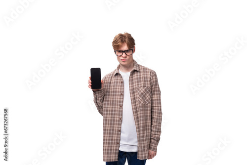 young stylish man with red hair dressed in a summer shirt shows a phone with a mockup photo