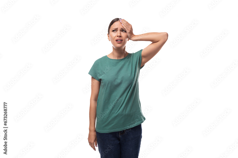 young forgetful brunette woman dressed in a green t-shirt on a white background - obrazy, fototapety, plakaty 