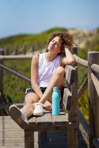 Fototapeta Naklejka Na Ścianę i Meble -  Happy young woman resting on wooden bench in sunlight