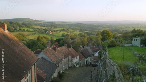 Gold Hill Shaftesbury.  Location of iconic Hovis Bread commercial by Ridley Scott. Evening sunshine on a summers day, steep cobbled street in rural England. Drone jibs down from high view. photo