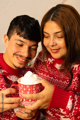 young cheerful couple holding christmas cup of chocolate with cream on christmas eve