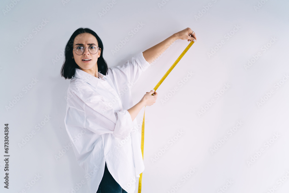 Puzzled woman measuring with meter tape Puzzled woman measuring with meter tape