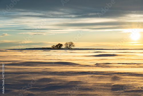 Winter snow blows across a frozen prairie lake at Lake Newell Alberta Canada under a sunset sky.