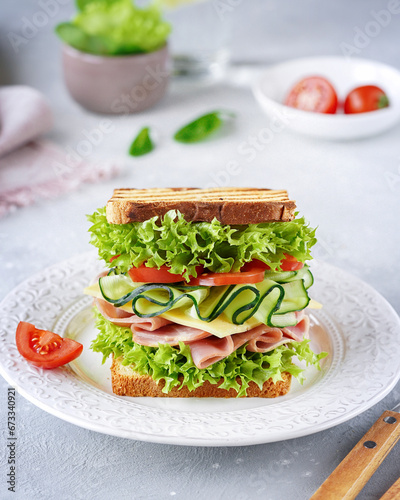 sandwich with bread with green salad, tomatoes, cheese, ham close-up, light background