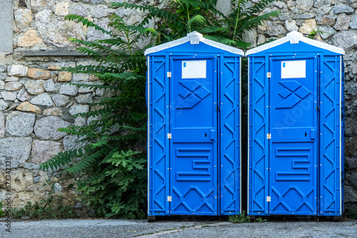 Public portable bio WC cabins by stone wall on city street. Mobile toilets installed for guests in urban park. Blue sanitary units in town photo