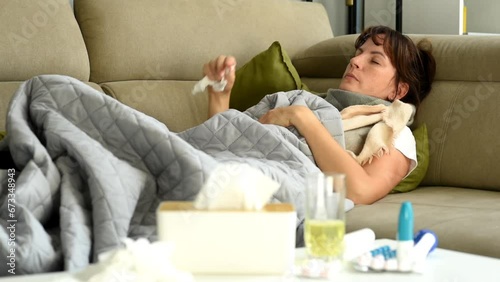 A middle-aged woman is lying on the sofa, experiencing fever, chills and signs of illness.  Illness and poor health at home