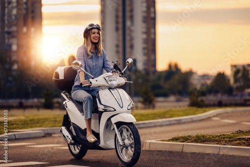 Cheerful young woman driving scooter in the city photo