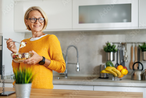Attractive mature woman eating salads in her kitchen