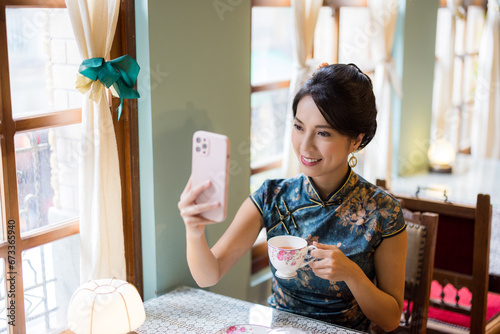 Woman wear traditional chinese cheongsam and use of mobile phone to take photo in the vintage restaurant photo