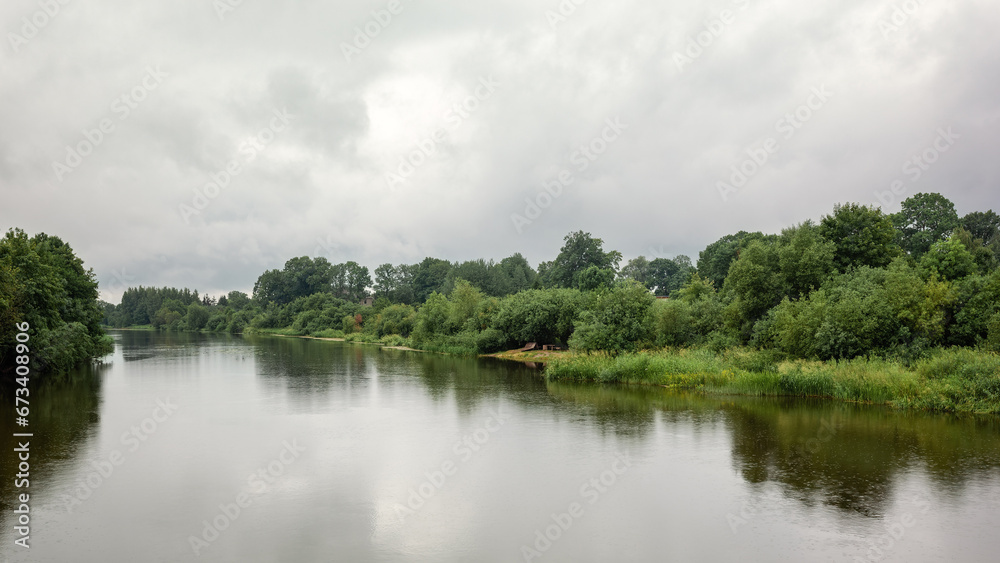 Lithuanian river on the banks of green foliage, view on a cloudy day with light rain