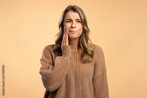 Obraz na plátně Unhappy sad woman holding hand on   cheek having a toothache, need medical treatment isolated on beige background