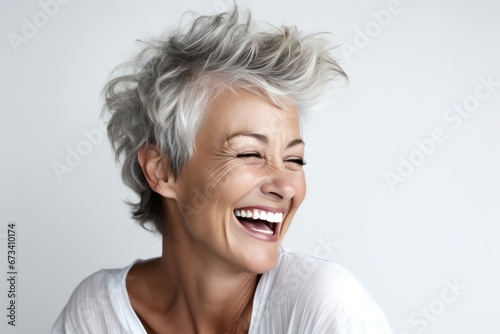 Joyful senior woman with stylish grey hair laughing heartily against a light background