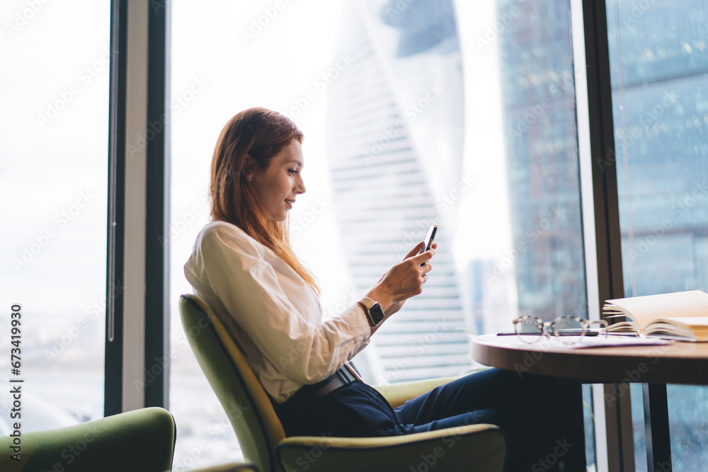 Smiling woman sitting at office table with smartphone in modern workspace