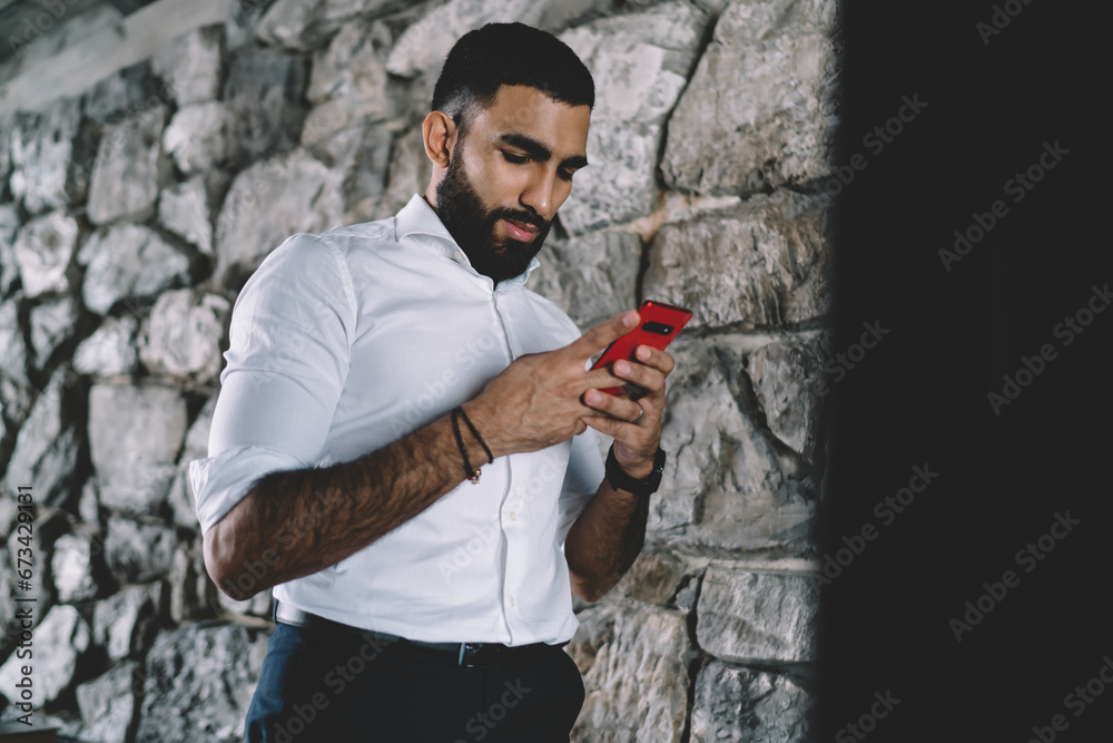 Confident man messaging on smartphone near stone wall