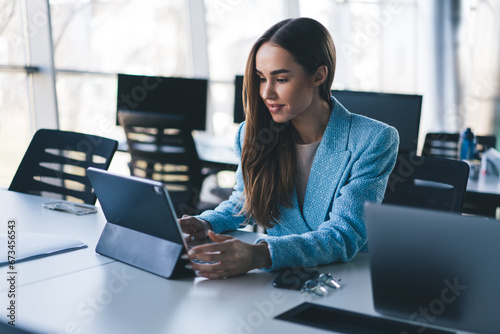 Positive young woman working on tablet and laptop in office