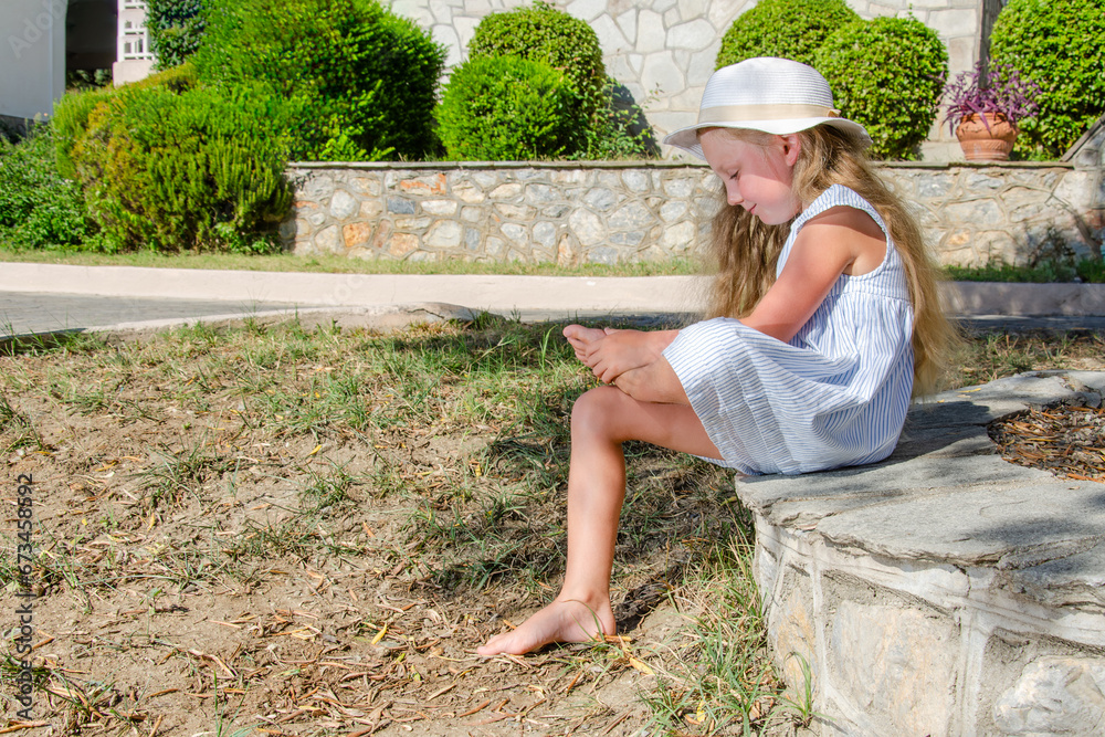 Obraz premium girl child sitting barefoot on stone bench.
