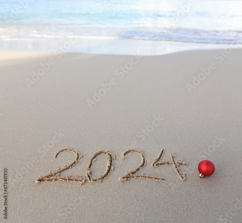 New Year 2024 background with Christmas ball and handwritten in the white sand.