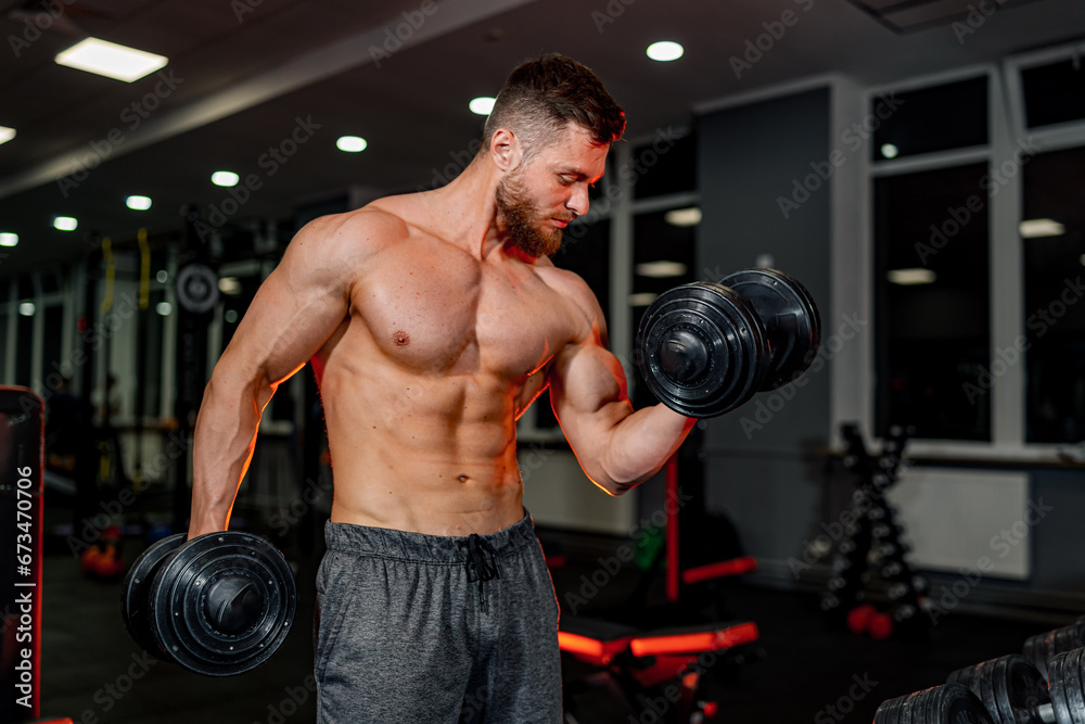 A Strong and Fit Man with Muscles Flexing in a Well-Equipped Gym. A shirtless man holding two dumbs in a gym A Strong and Fit Man with Muscles Flexing in a Well-Equipped Gym. A shirtless man holding two dumbs in a gym