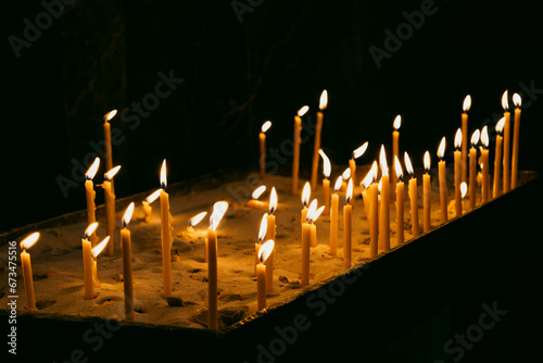 Many burning tall wax candles with bokeh light background. Catholic or Orthodox church. Flame of candles in the dark sacred interior of the temple. Religious tradition. Prayer and Christian Faith