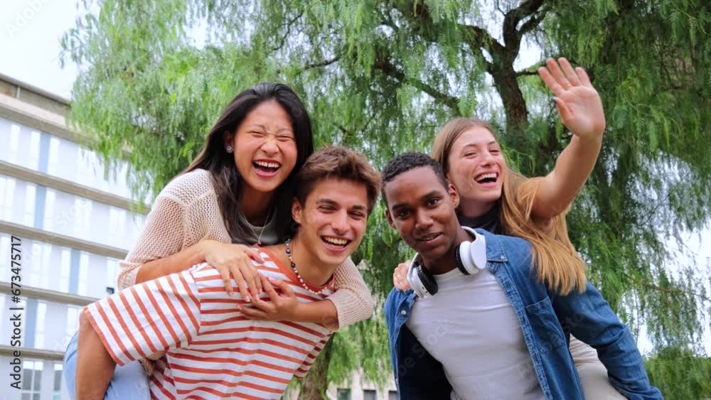 Two multiracial teenage student best friends giving a piggyback ride to their girlfriends. Young men smiling and having fun carrying women on his shoulders waving hands and looking at camera together Two multiracial teenage student best friends giving a piggyback ride to their girlfriends. Young men smiling and having fun carrying women on his shoulders waving hands and looking at camera together
