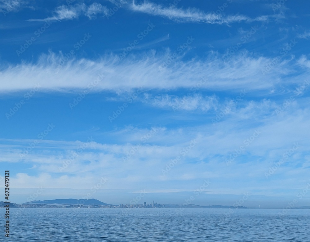 distant view of San Francisco across the bay, framed by a clear blue sky and scattered clouds distant view of San Francisco across the bay, framed by a clear blue sky and scattered clouds