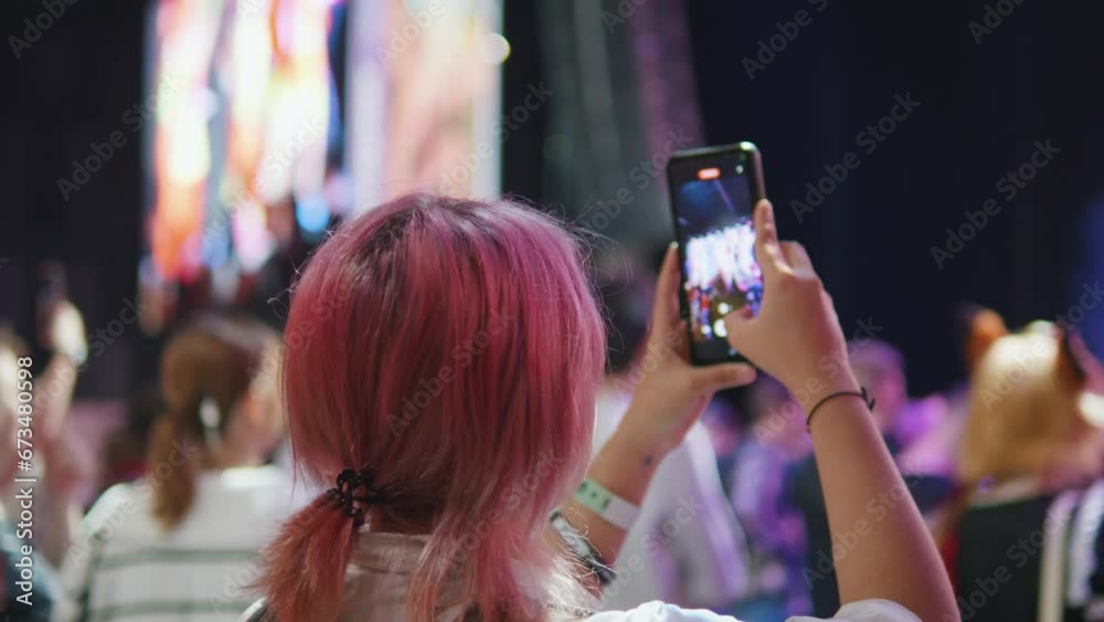 Girl takes video on phone at music anime cosplay gaming convention concert.