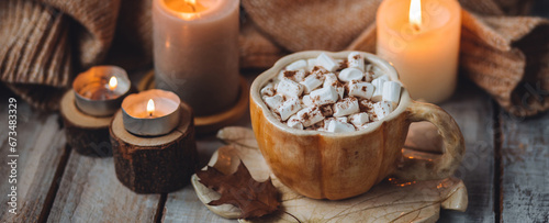 Spicy sweet fall hot drink: delicious pumpkin latte with cinnamon, marshmallow with salted caramel. Served in handmade artisan mug in shape of pumpkins, cozy home decor with candles, dry autumn leaves