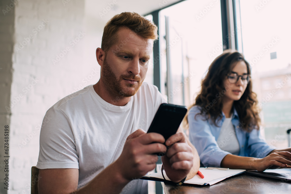 Young couple sitting at table and using smartphone and laptop in cafe Young couple sitting at table and using smartphone and laptop in cafe