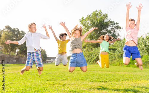 Happy school children jumping on the green lawn in summer park