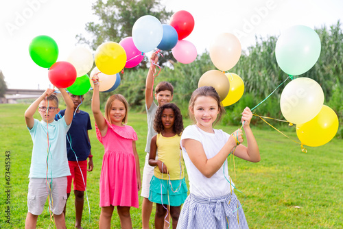 Joyful barefoot kids having fun together while playing with balloons on field.