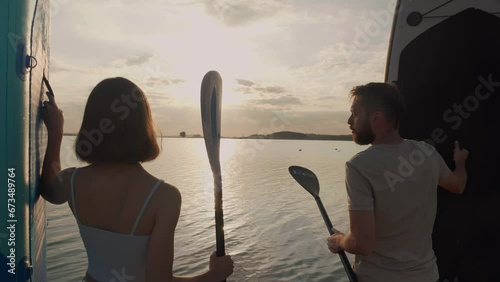 Happy couple preparation for paddle boarding at lake during sunset together Back view. Healthy people enjoy outdoor active lifestyle play extreme sport surfing on summer vacation. photo