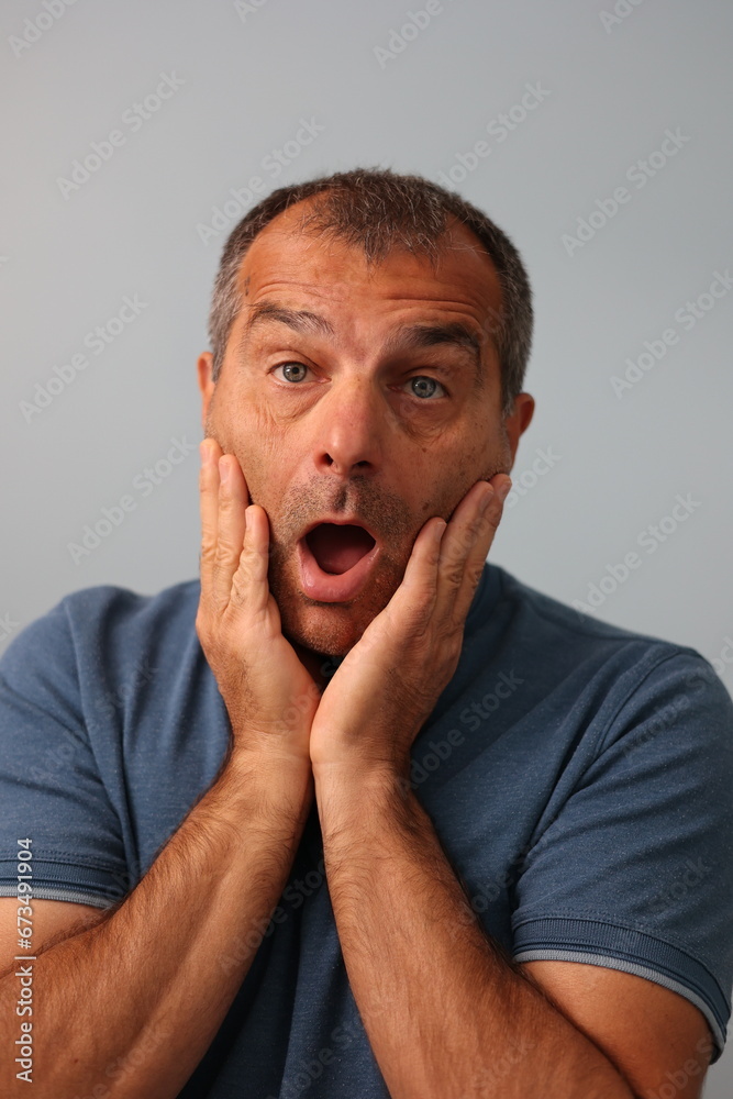 Close up studio portrait of surprised or astonished mature man with both of his hands on his chicks Close up studio portrait of surprised or astonished mature man with both of his hands on his chicks