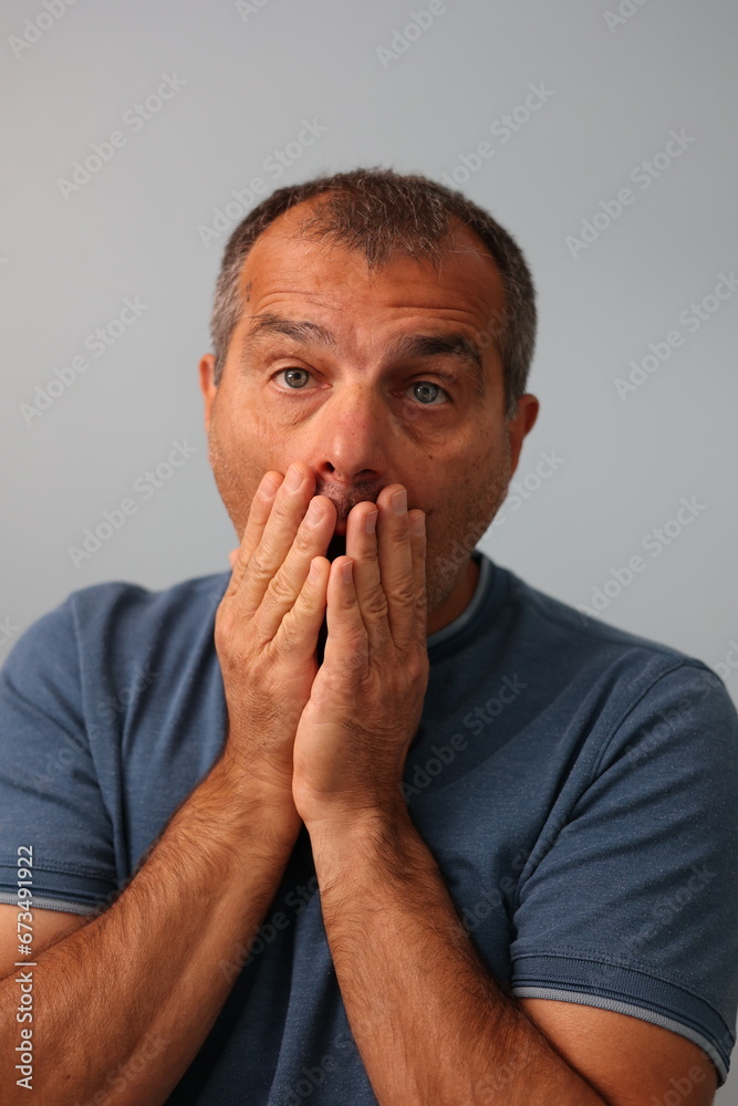 Close up portrait of mature man covering his mouth with both hands in an expression of disbelieve and surprise Close up portrait of mature man covering his mouth with both hands in an expression of disbelieve and surprise