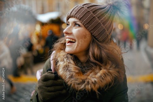 happy woman in green coat and brown hat at winter fair in city