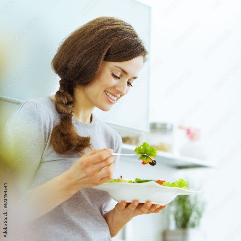 Young woman eating fresh salad in modern kitchen Young woman eating fresh salad in modern kitchen