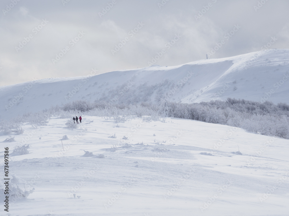 Winter mountain landscape. Mountain peaks covered with snow. View from Mala Rawka to Wielka Rawka. three tourists walking along a snow-covered trail.  Bieszczady Mountains. Poland
