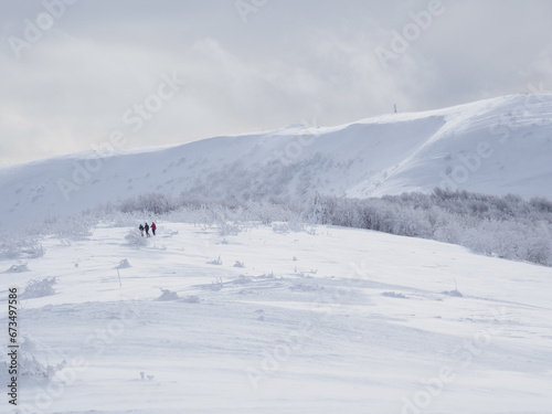 Winter mountain landscape. Mountain peaks covered with snow. View from Mala Rawka to Wielka Rawka. three tourists walking along a snow-covered trail. Bieszczady Mountains. Poland