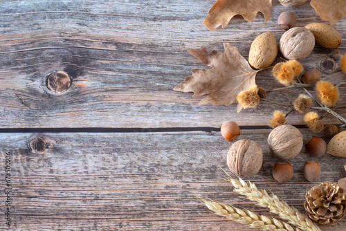 Autumn still life on wooden rustic background: dry leaves, wheat, and various nuts (walnut, almond, hazelnut). Top view, copy space. Fall harvest season concept.