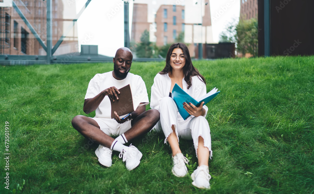 Fototapeta premium Positive multiethnic students studying on grass in park