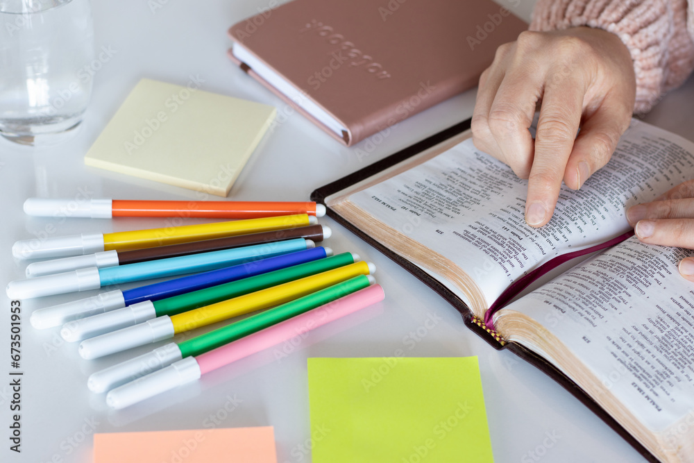 Hand holding open holy bible book and pointing to inspiring verse. Christian biblical study, reading, writing, taking notes with colorful markers at home concept. Hand holding open holy bible book and pointing to inspiring verse. Christian biblical study, reading, writing, taking notes with colorful markers at home concept.