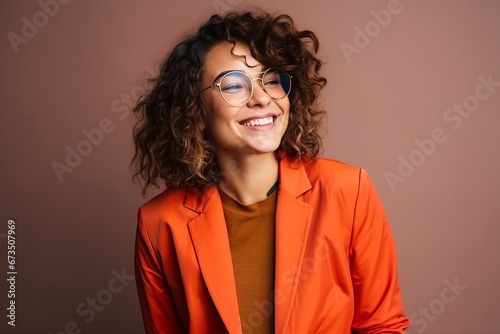 Portrait of beautiful young woman with curly hair wearing orange jacket and glasses