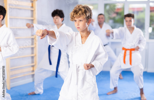 Willing junior boy wearing kimono training karate techniques in group during workout session