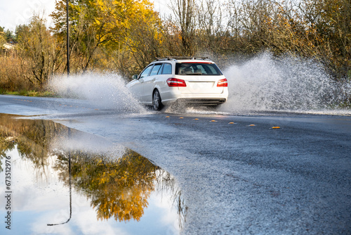 After the storm, white car splashing through rainwater flooding over a residential street on a sunny fall day 