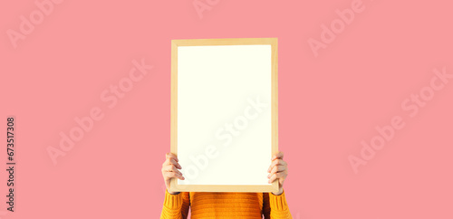 Portrait of woman holding and showing blank a photo frame mockup on pink studio background
