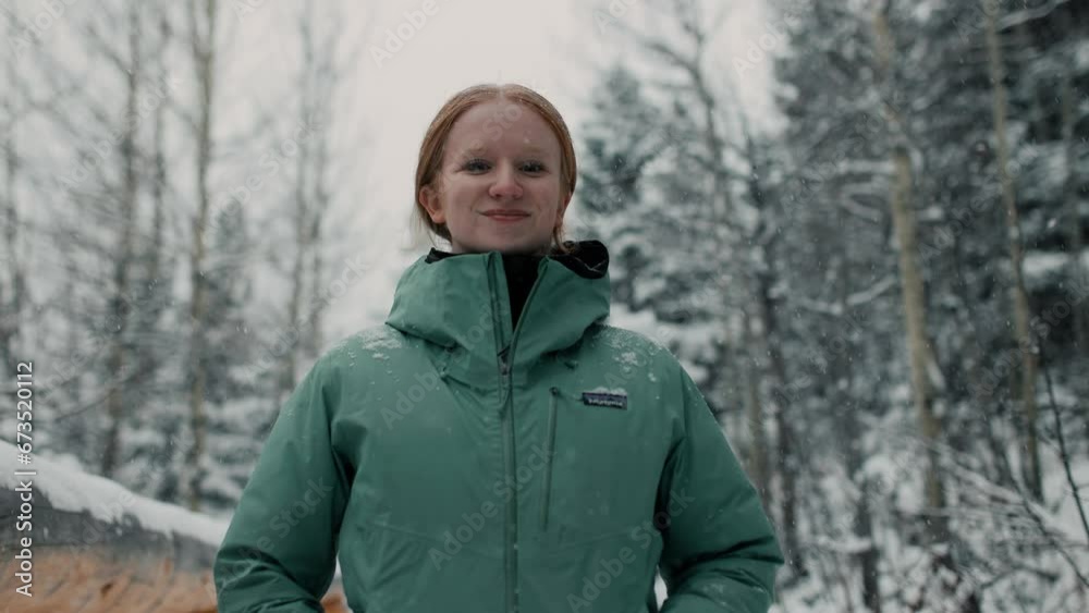 female hiker stops, looks around, and smiles to camera as snow falls in the mountains around her female hiker stops, looks around, and smiles to camera as snow falls in the mountains around her