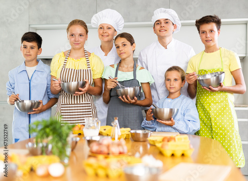 Young guy and adult woman cook posing with group of children at cooking master class