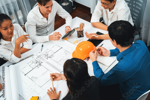 Diverse group of civil engineer and client working together on architectural project, reviewing construction plan and building blueprint at meeting table. Prudent