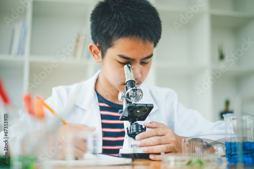 Asian male science students looking through a microscope and tests of plants in the classroom. Learning about scientific experiments on plant species.