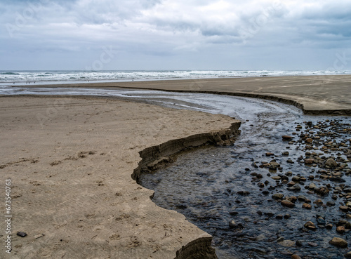 A creek flows into the Pacific Ocean on an overcast day near Yachats, Oregon, USA