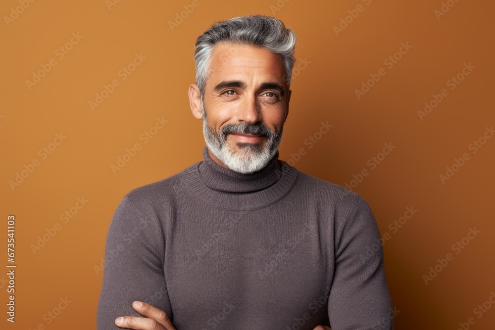 Confident mature man with grey hair and beard. Confident mature man looking at camera and smiling while standing against orange background